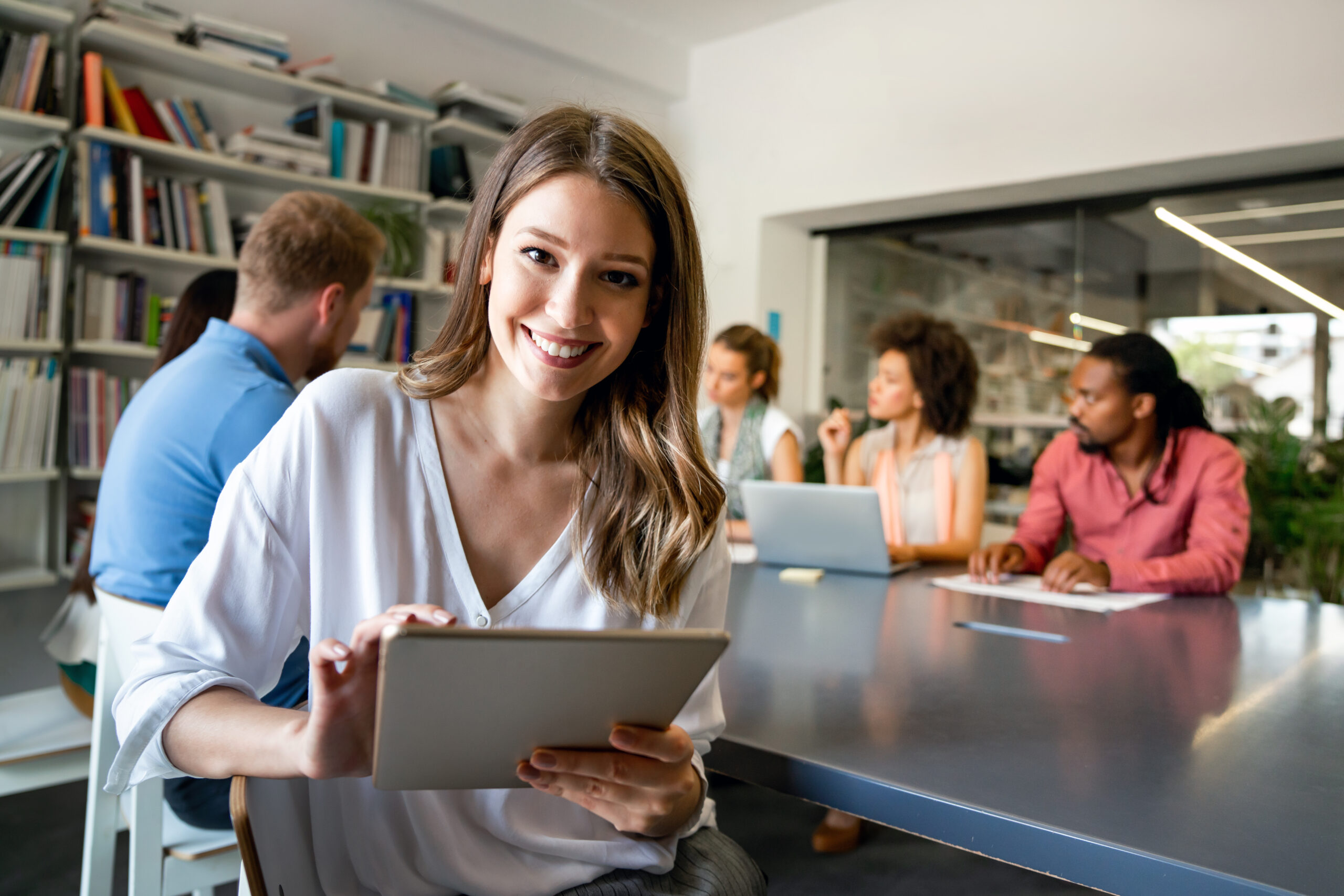 Mujer sonriendo consultando una tablet con gente reunida de fondo